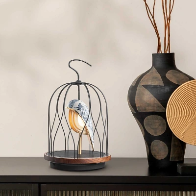 Ein DaqiConcept Jingoos in einem schwarzen K&auml;fig, verziert mit einem bemalten Blumendesign auf Keramik und goldenen Details. Rechts daneben steht eine gro&szlig;e Vase. Alles auf einer dunklen Kommode, vor einem beigen, sanft strukturierten Hintergrund.