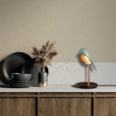 Auf einer K&uuml;chenablage aus weissem Stein steht die Bird-Lampe aus gr&uuml;nem Porzellan mit goldenen Details auf einem Walnussholz-Sockel. Daneben schwarzes Geschirr und eine Vase mit beigen Trockenblumen vor gelblich-beiger Wand.