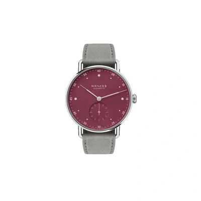 Frontansicht Nomos Metro: Klare, moderne Gestaltung mit feinem Minutendruck und dezenten Punktindizes. Die schlanken, nadelartigen Zeiger in Silber und pink setzen elegante Akzente. Ein muted red Zifferblatt mit technischer Raffinesse und Leichtigkeit.