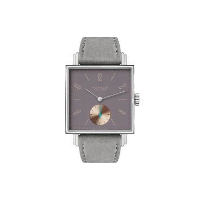 Nomos Tetra mit markant eckigem Design und violetten Zifferblatt. beigen Strichindizes und arabische Zahlen sorgen f&uuml;r klare Ablesbarkeit. Die kleine Sekunde bei 6 Uhr tr&auml;gt einen blauem Zeiger. Einem grauen veganen Veloursband rundet den Look ab.